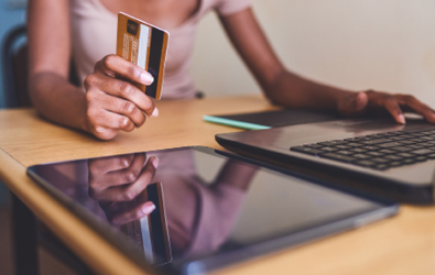 woman holding a credit card in one hand and clicking on a key of a laptop with the other