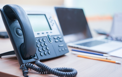 phone handset with system on a desk beside a laptop and pencils