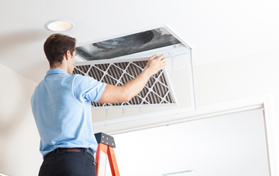 person on a ladder installing a new air filter over ceiling duct