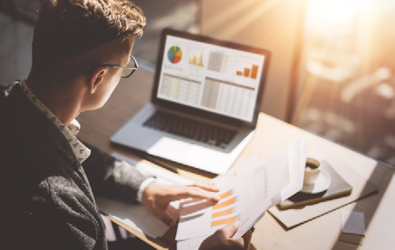 person looking at a laptop displaying charts and graphs, while holding a bar graph report