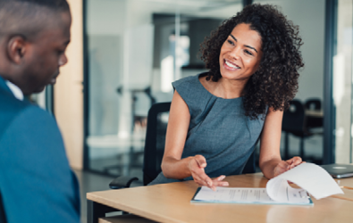 woman at desk looking through a document with man also sitting at end of desk