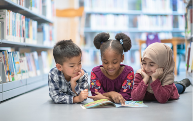 three kids on the floor of a library reading a book together
